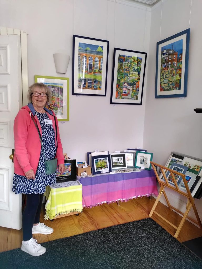 Helen standing next to some of her paintings displayed on the wall of a house as part of Art House 2024.